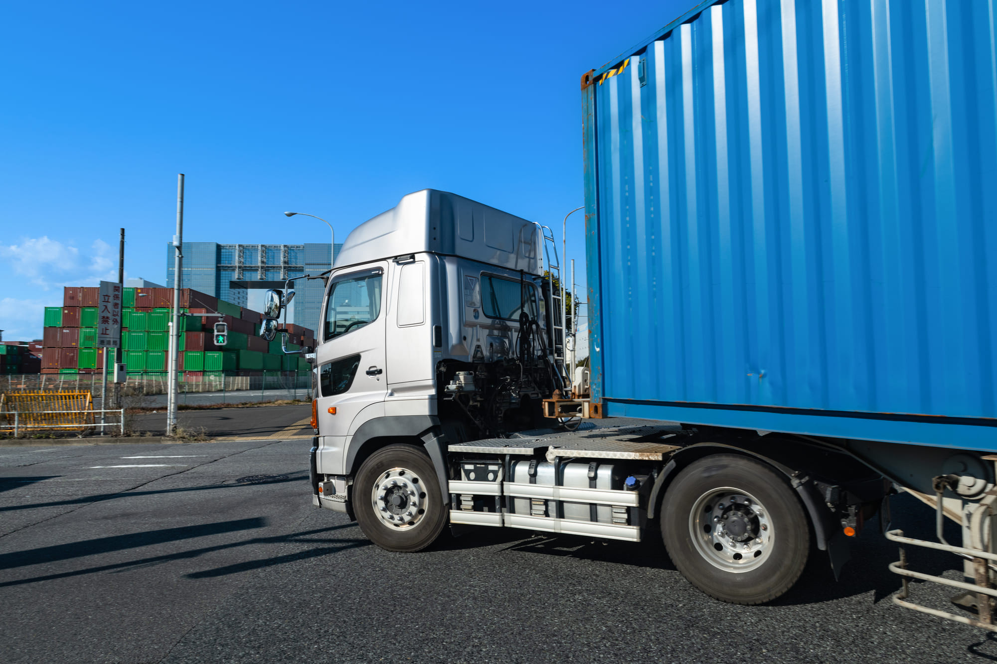 Truck hauling a blue shipping container at a freight yard under a clear sky.