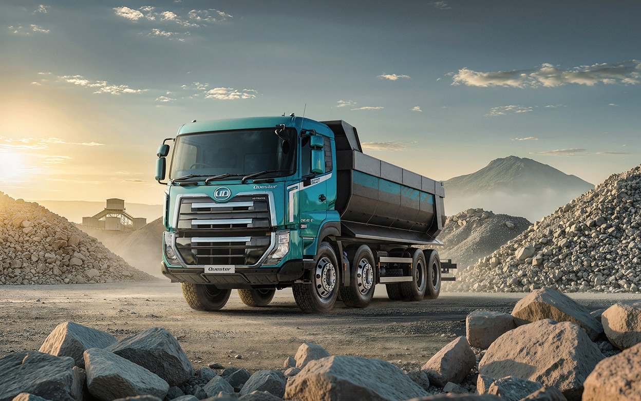 Blue dump truck on a gravel lot at sunrise, surrounded by rocky mounds.