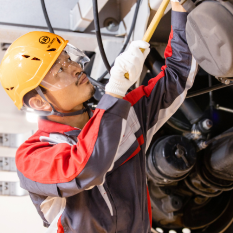 Worker in a safety helmet repairs machinery, focused and wearing protective gear.