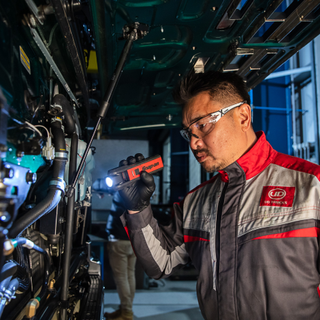 Man inspects machinery with a flashlight, wearing safety glasses and a work uniform.