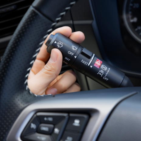 Hand turning a car's windshield wiper control lever on the steering wheel.