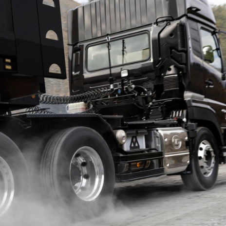 黒い大型トラックが煙を上げて発進している。