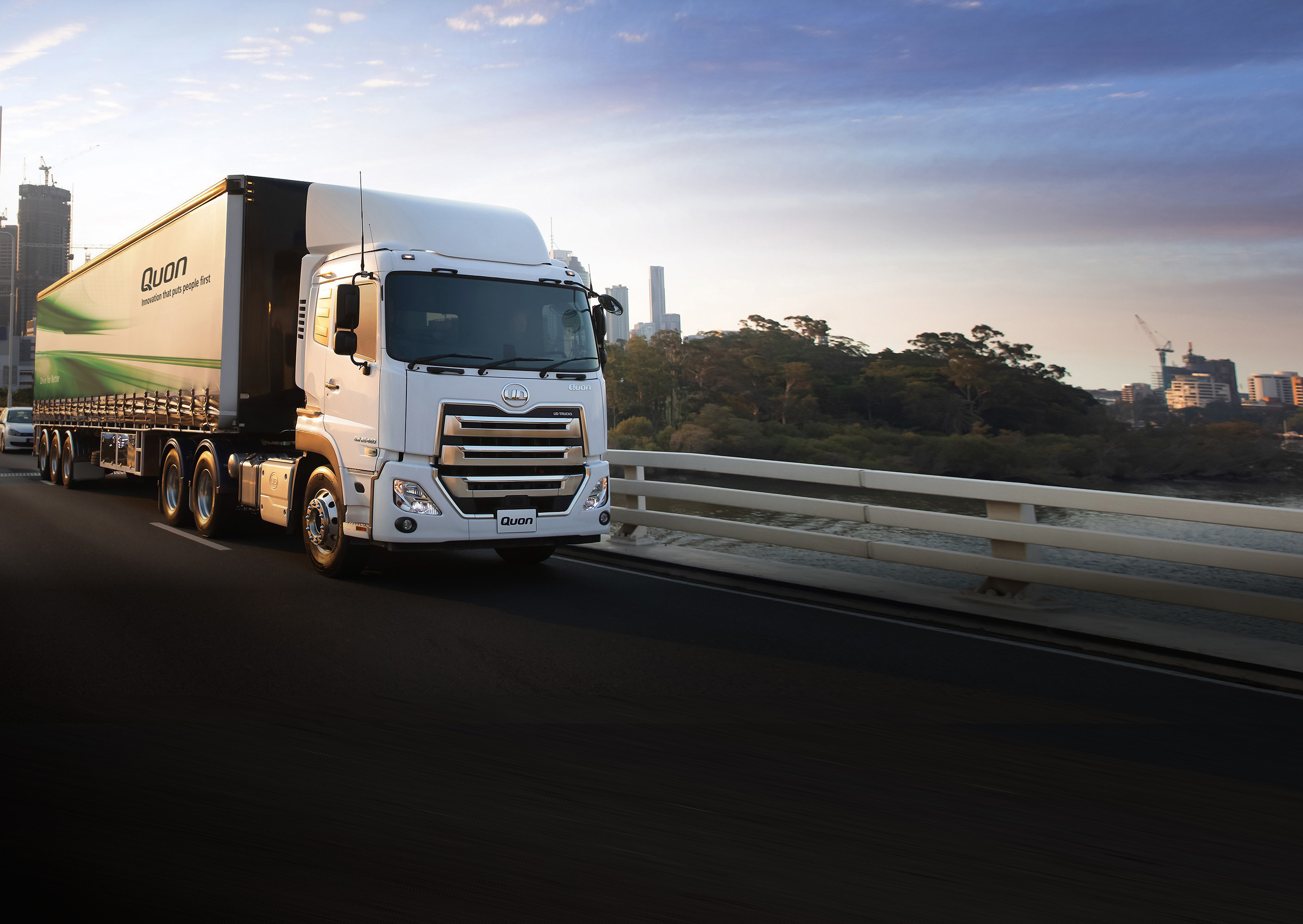 Large white semi-truck with green stripes driving on a bridge at sunset.