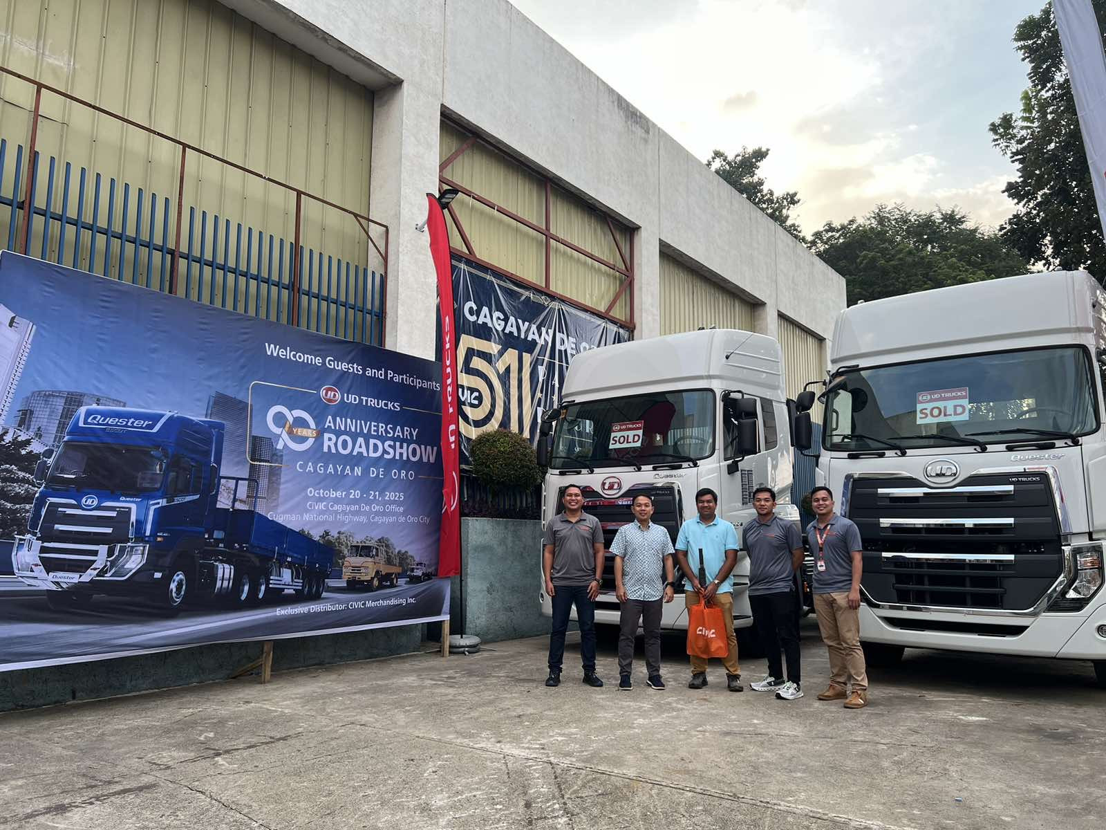 Limang tao sa harap ng dalawang puting trak sa labas ng gusali