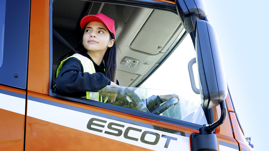 Woman in red cap and safety vest driving an orange truck labeled ESCOT.