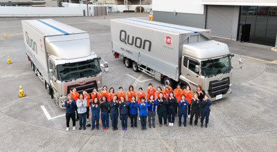 二台の大型トラックの前で並んでポーズをとる作業員たち