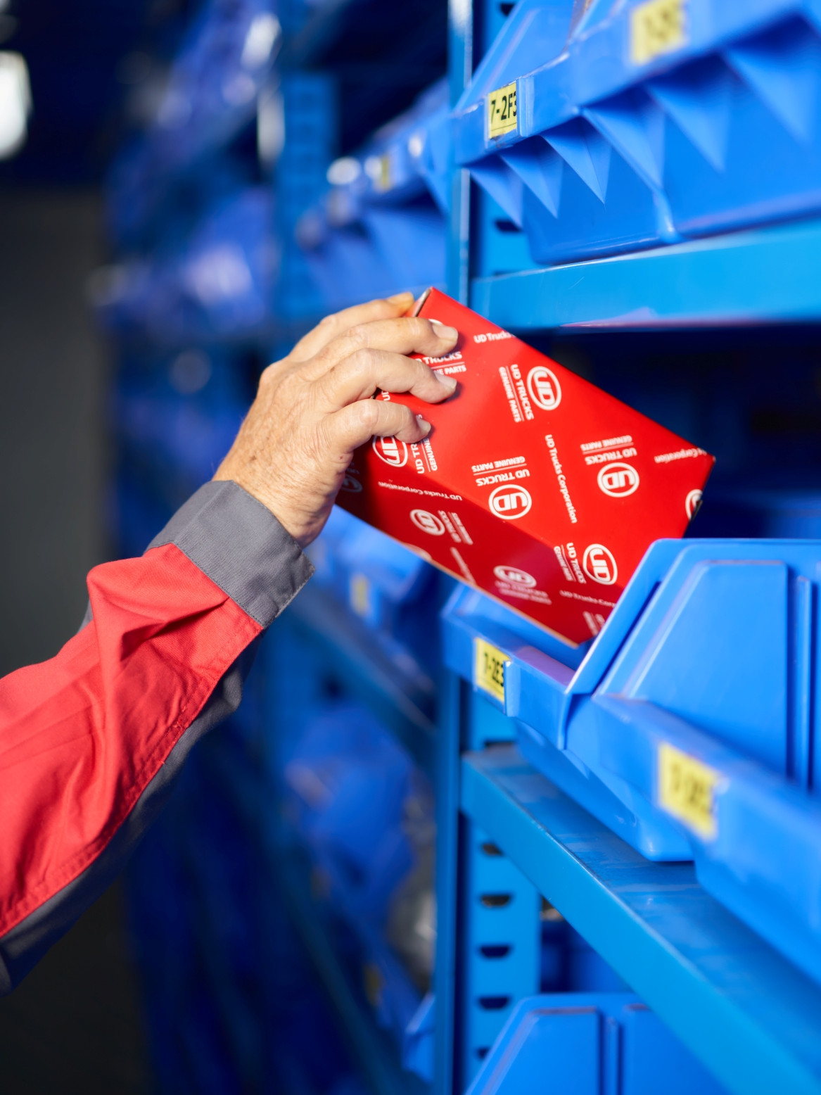 Hand placing genuine UD Trucks parts into blue shelving unit.
