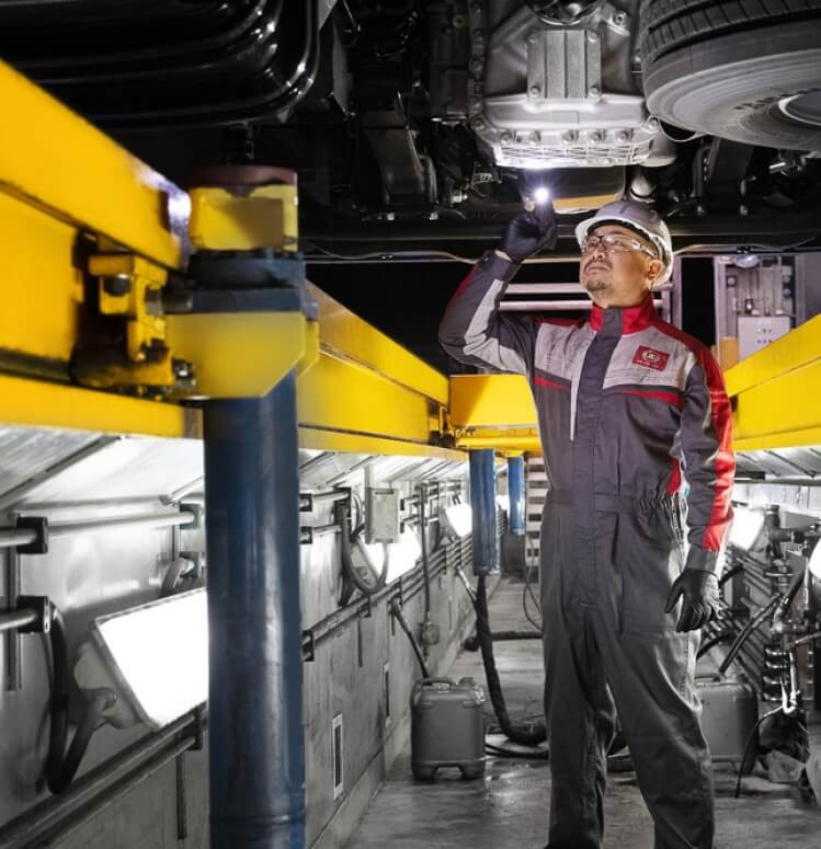 Monteer inspekteer voertuigonderstel met flitslig in verligte werkswinkel.