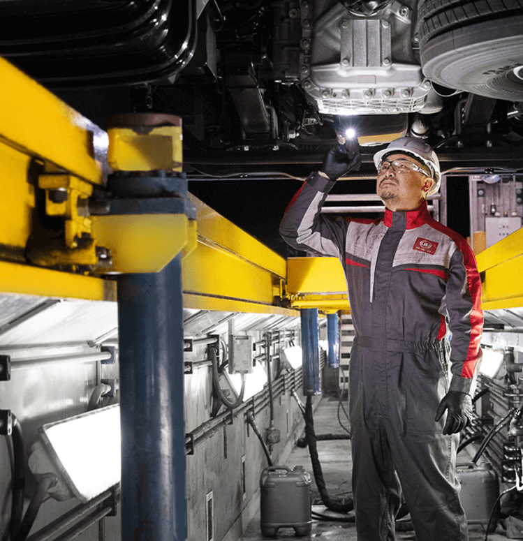 Mechanic in uniform inspecting vehicle underside with flashlight in a workshop.
