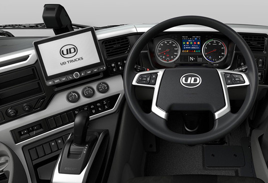Truck dashboard with digital screen, gauges, and steering wheel displaying UD logo.